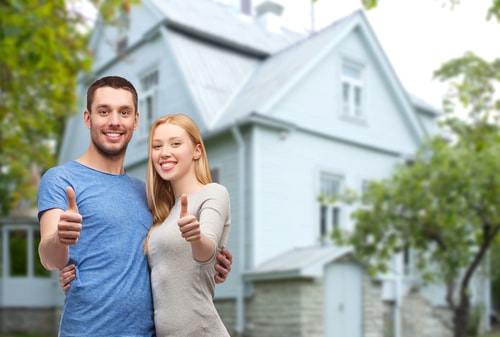 smiling couple hugging and showing thumbs up over house background
